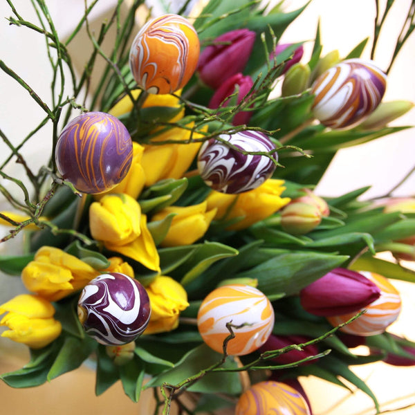 <img src=“Osterstrauß.png” alt=“Osterstrauß mit gelben und violetten Tulpen, gebunden mit Ostereiern”>